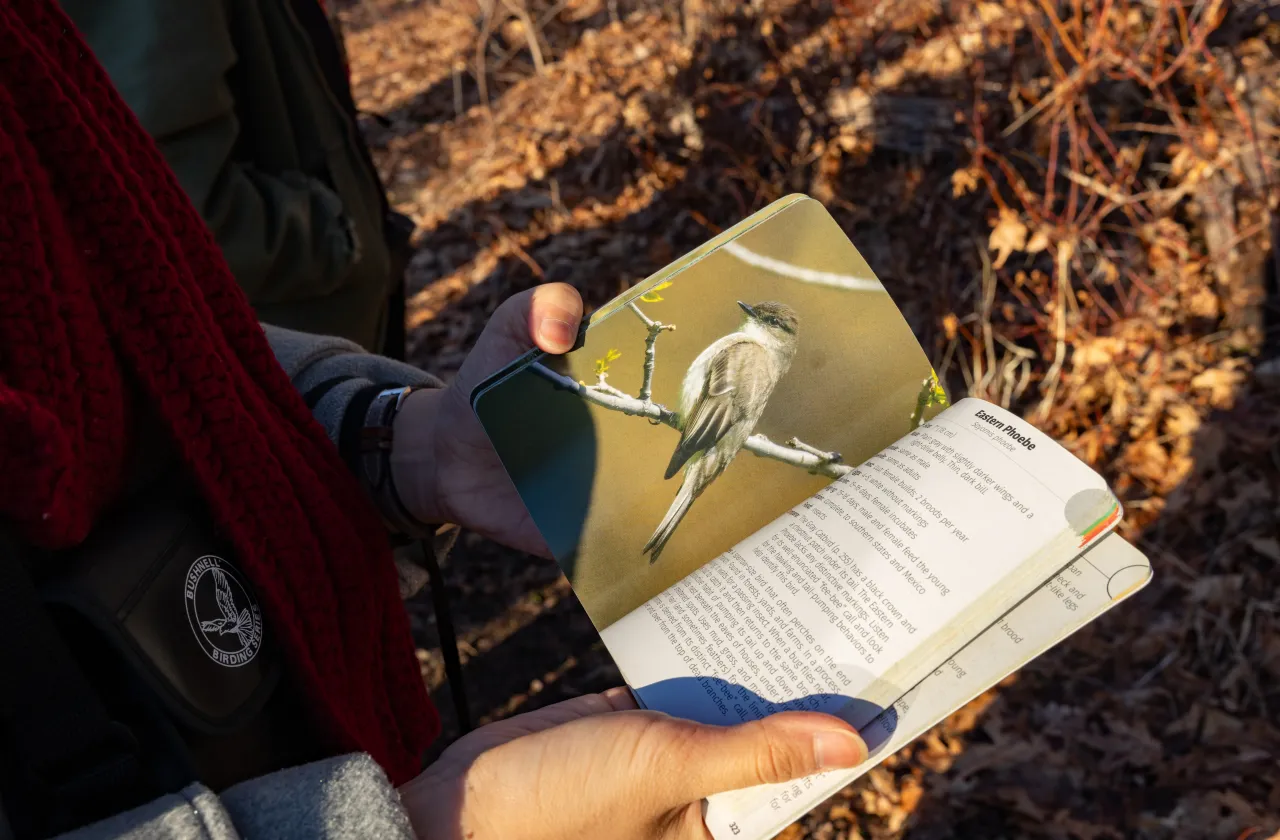 A student holds open a book with an illustration of a bird inside.