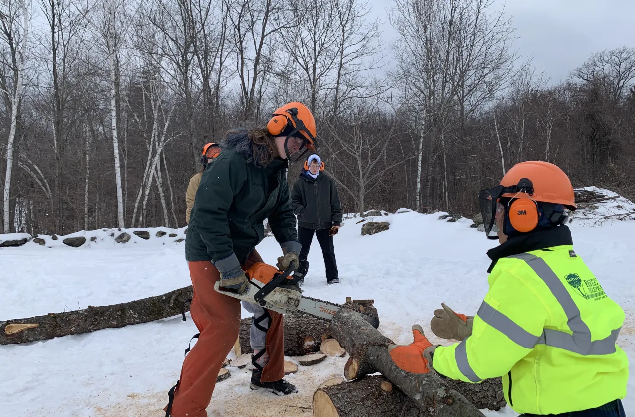 Students use a chain saw to cut up a fallen tree.
