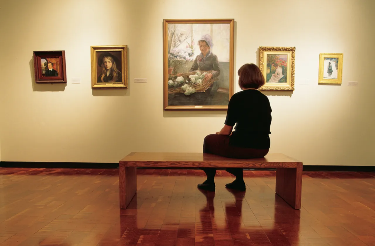 museum goer sitting on a bench taking in a painting of a girl