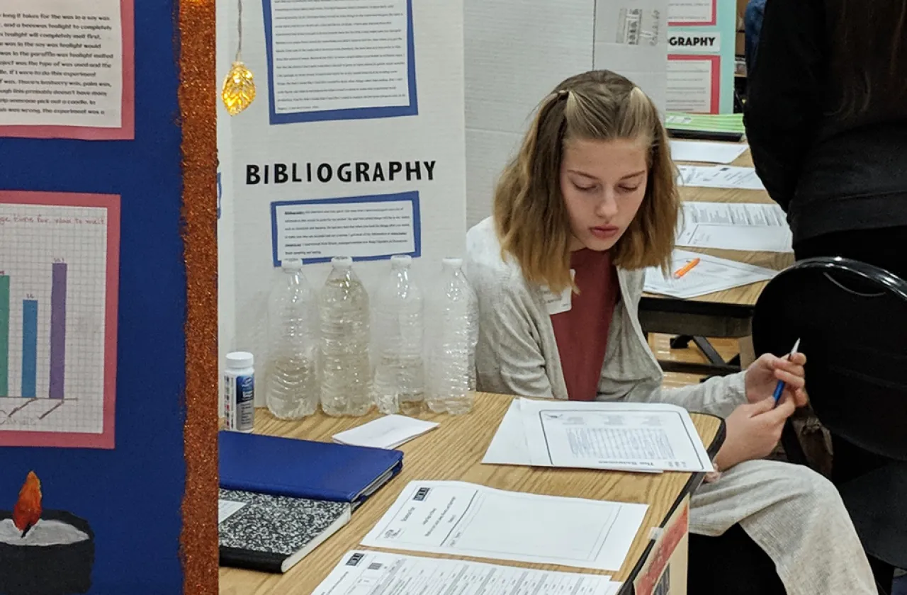 Student studying her notes at her booth during a science fair