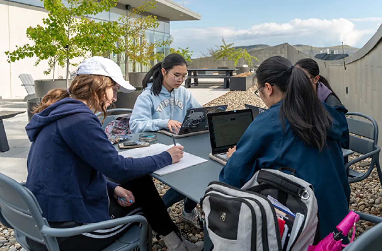 Four students studying and sitting around a table together, outside on the roof of Neilson library.