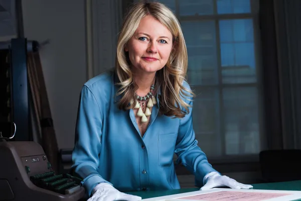 Dorothy Moss wearing gloves with documents on a table in front of her, looking into the camera with a slight smile