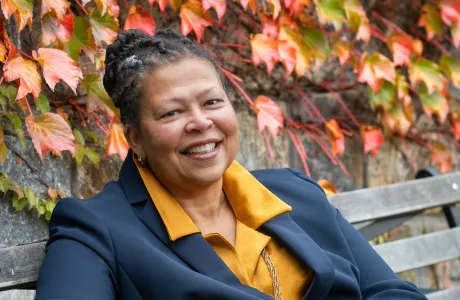 Sarah Willie-LeBreton smiling outdoors and sitting on a bench, cropped and close up.