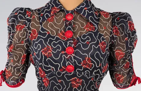Photo of a sheer, button-up, navy blue, collared top with red buttons and elaborate pattern consisting of wavy white lines and red flowers.