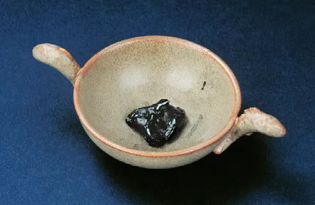 A tan ceramic bowl with two small handles contains a glossy, dark substance at its center