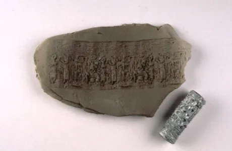 A clay tablet with intricate carvings depicting human figures and animals, next to a cylindrical seal with similar designs