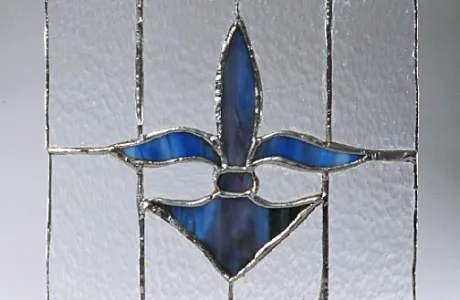 Stained glass panel with a blue fleur-de-lis centerpiece. The background is textured with clear glass, framed by a border of red and blue diamonds.