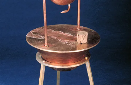 An antique, copper steam engine model features a spherical chamber, curved tubes, and stands on three legs