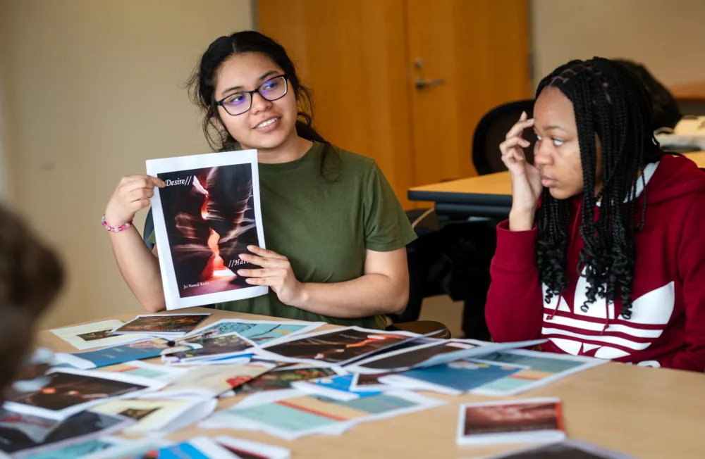 A student holds up a photo of a chapbook cover