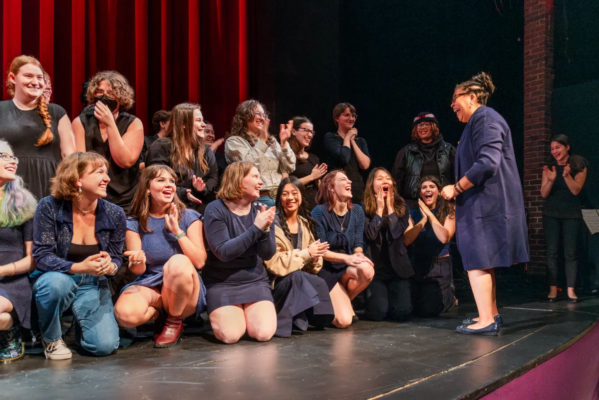 A group of students on the stage in Mendenhall, clapping and smiling as Sarah Willie-LeBreton greets them