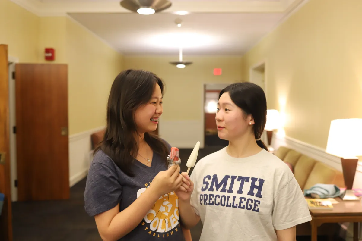 Two students smile at each other while holding popsicles.