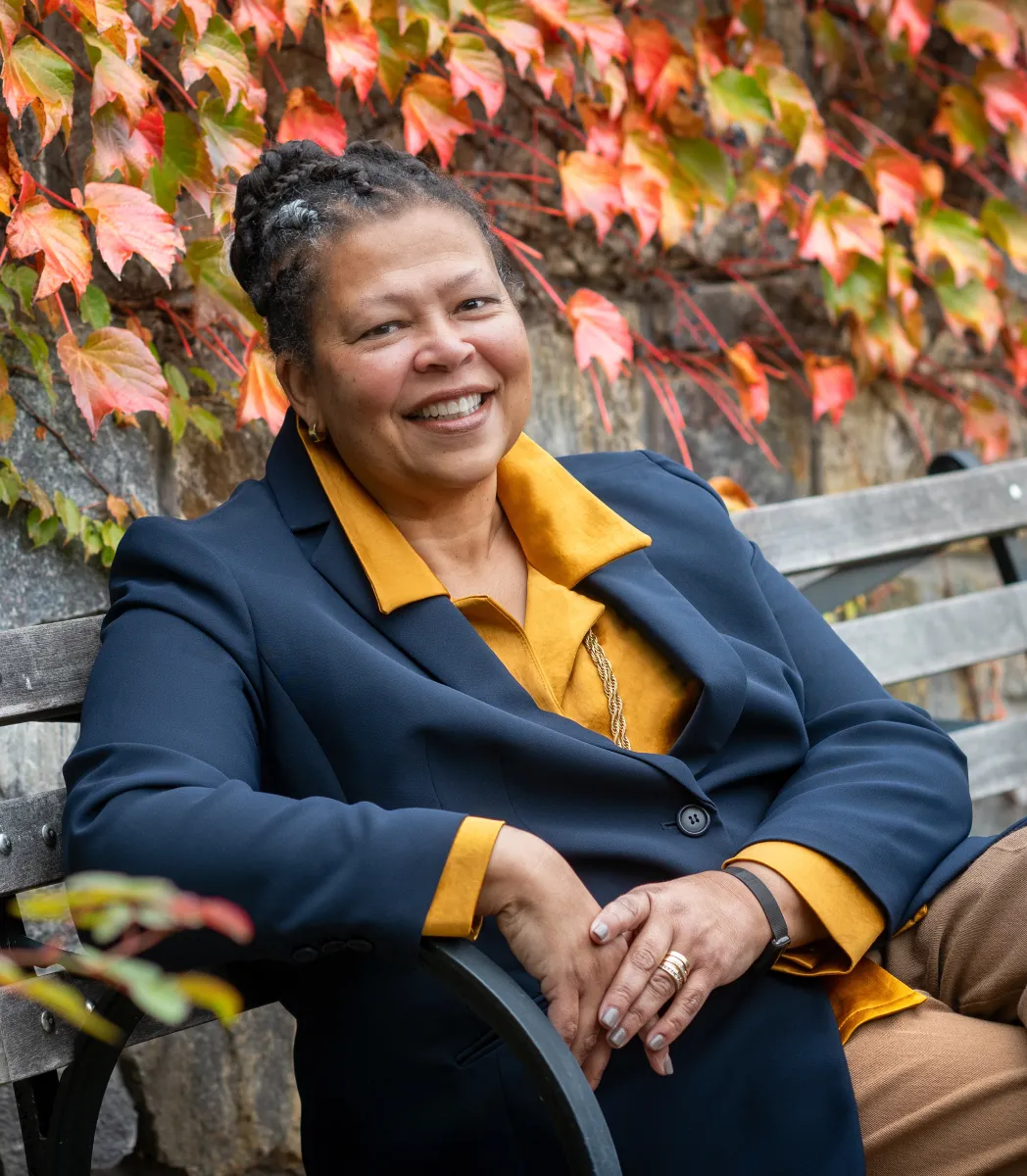 Sarah Willie-LeBreton smiling outdoors and sitting on a bench, cropped and close up.