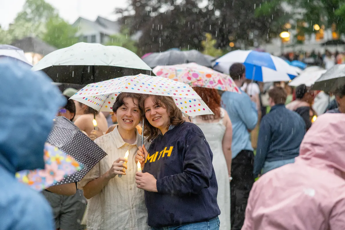 A senior and a guest stand underneath a polka-dotted umbrella in the rain during Illuminations