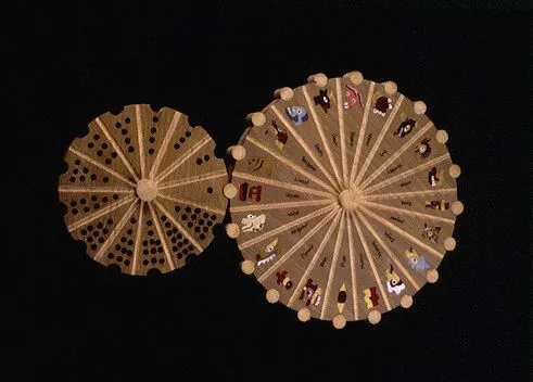 Two wooden circular objects with radial patterns are displayed. The larger wheel features astrological symbols, while the smaller one shows arranged black dots.