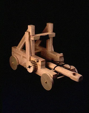 A wooden model catapult features detailed gears, wheels, and a launching arm