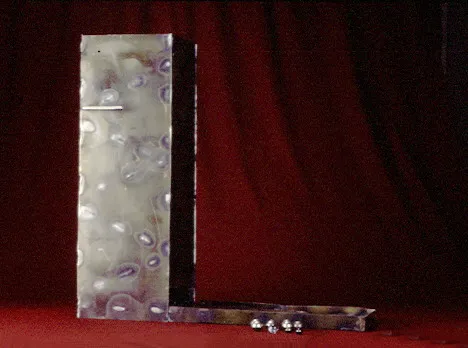 A tall, abstract metal sculpture with three small metallic balls at its base