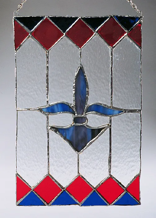 Stained glass panel with a blue fleur-de-lis centerpiece. The background is textured with clear glass, framed by a border of red and blue diamonds.