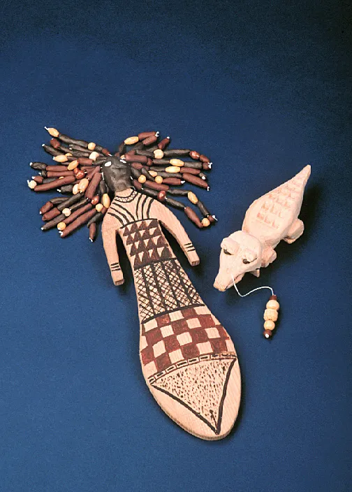 Wooden doll with bead hair and a dress with geometric patterns lies next to a carved crocodile