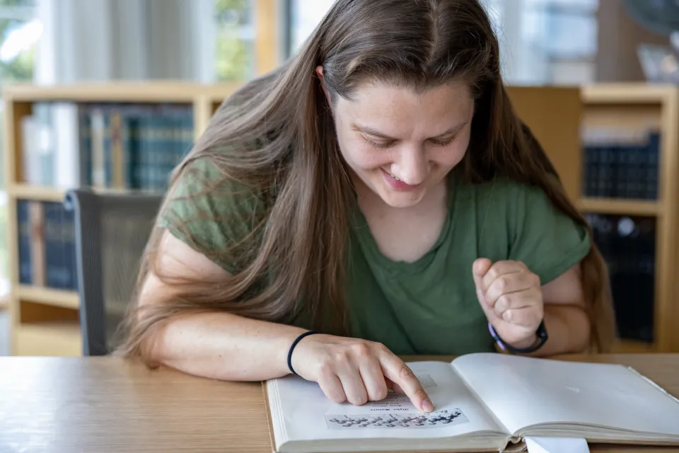 Kady Wilson smiles while looking at an old yearbook in Special Collections