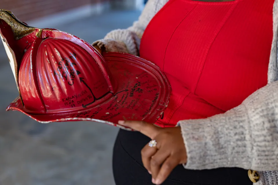 Diamond Jones' hand pointing to names on the red Comstock fire helmet