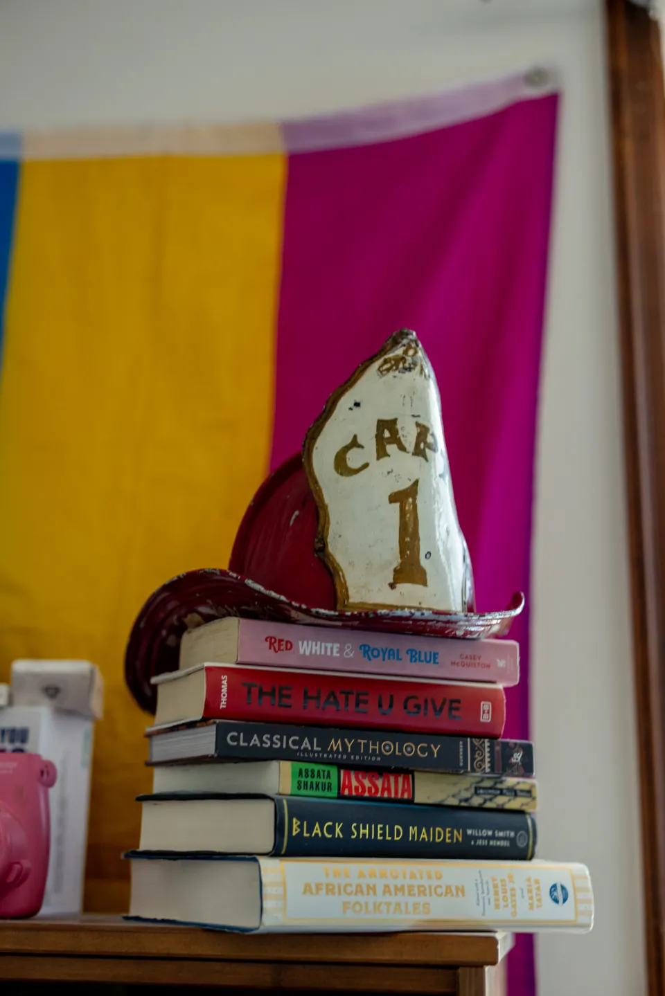 The Comstock's red fire captain helmet sits on a stack of books on a bureau in front of a colorful flag