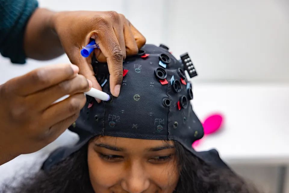 Student researcher Kris Cheaye fits an fNIRS cap to Gloriamar Esteves’s head