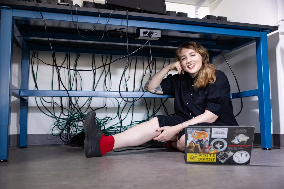 Goldwater Scholar Mary-Alice Wieland poses underneath a table in the computer lab with her laptop at the ready