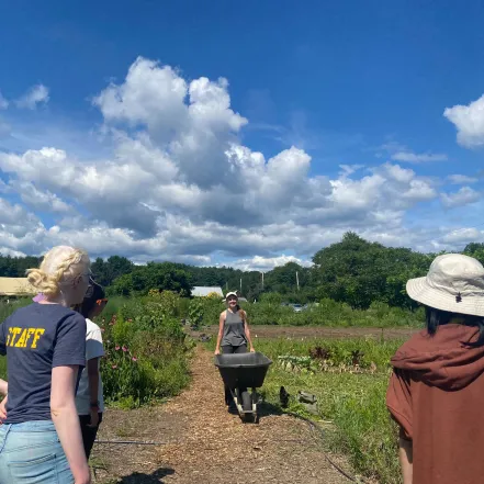 Students in a field with a wheelbarrow.