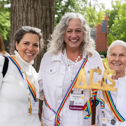 Ada Comstock Scholar alums wear white with rainbow-colored sashes and smile at the camera during Reunion